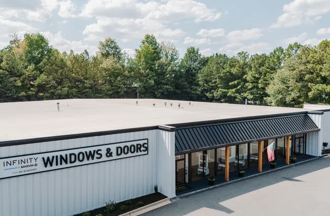 Exterior view of Infinity Windows & Doors store with trees in background and clear sky above.