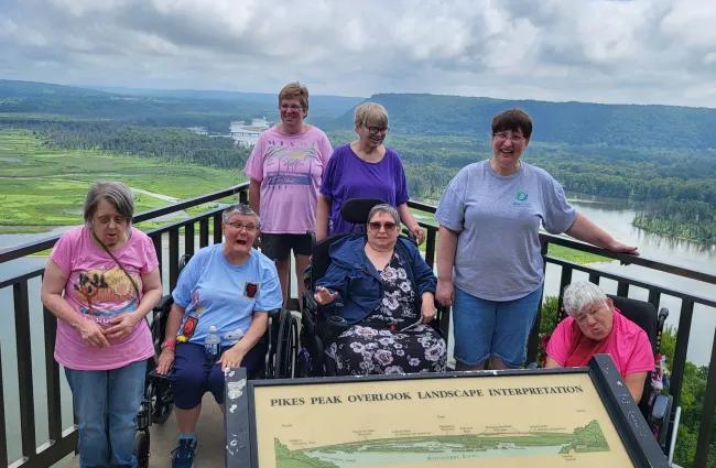 A group of cheerful individuals with disabilities poses at Pikes Peak Overlook, enjoying scenic river views.