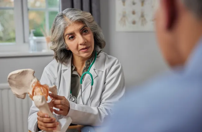 Female doctor explaining hip joint anatomy to patient using a pelvis bone model in clinic.