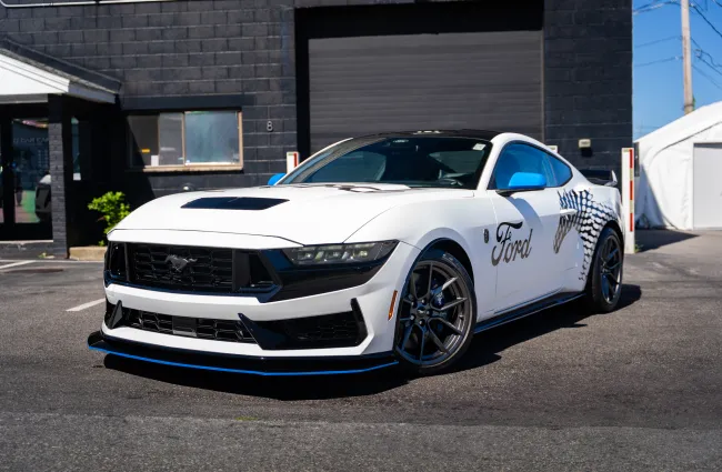 White Ford Mustang sports car with custom black and blue accents parked in front of a black building.