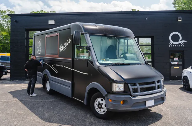 Black food truck with Racoo's branding being cleaned outside a black building with Q Car Care logo.