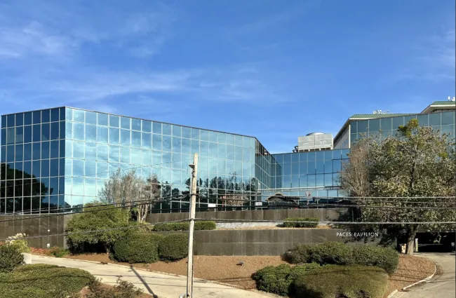 Modern glass office building reflecting blue sky with surrounding greenery and clear weather conditions