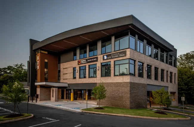 Modern three-story office building with large windows, brick facade, and signs for medical and orthopedic clinics.