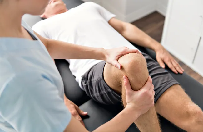 Physical therapist examining and stretching a patient's knee during rehabilitation therapy session.