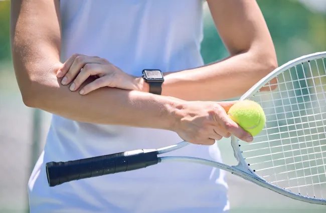 Person holding a tennis ball and racket, preparing to serve on an outdoor tennis court.