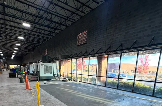 Spacious warehouse workshop with concrete floor, large windows, industrial machines, and safety cones.