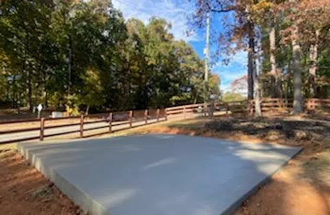 Newly poured concrete slab foundation in a wooded area under a clear blue sky with autumn trees.
