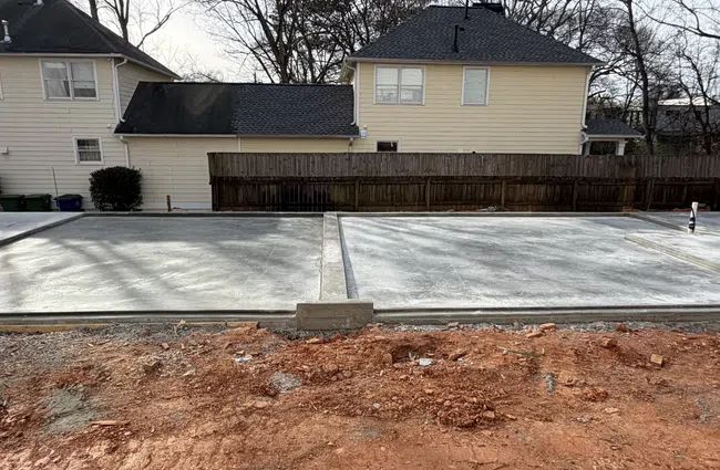 Freshly poured concrete slabs in a residential backyard with red soil and neighboring houses in the background