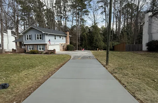 Newly poured concrete driveway leading to a two-story house with surrounding lawn and tall trees.
