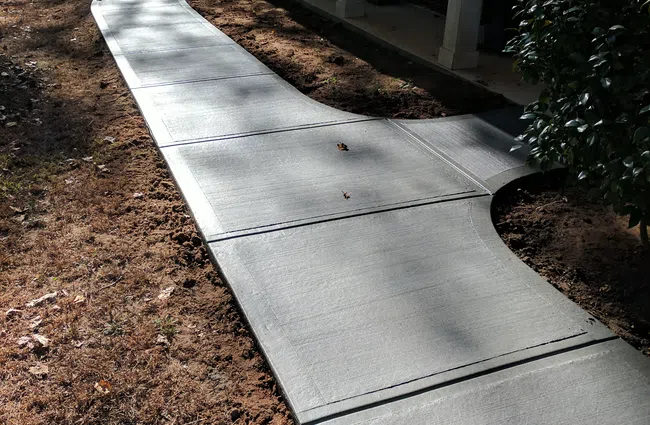 Newly poured curved concrete sidewalk leading to a house porch with caution tape and surrounding dry soil.