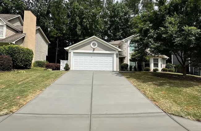 Freshly poured concrete driveway leading to a two-car garage with surrounding green lawn and trees.