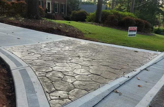 Stamped concrete driveway with a textured pattern in front of a brick house and green lawn.