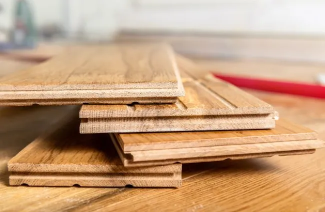 Stack of interlocking hardwood flooring planks laid on a wooden surface with blurred background.