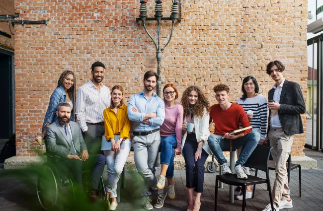 Diverse group of young professionals casually posing in front of a brick wall in a modern office patio