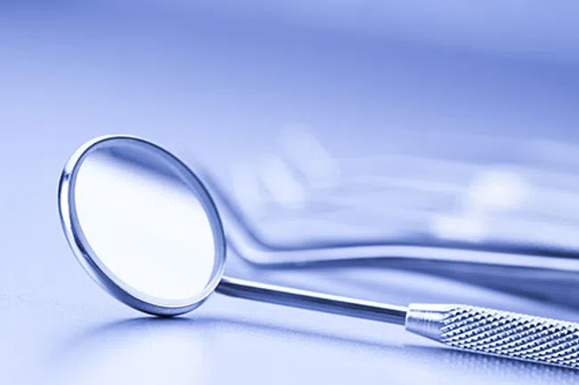 Close-up of a dental mirror with textured handle on a smooth surface with a blue tint background.