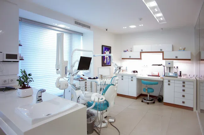 Bright modern dental clinic with dental chair, monitor, sink, and white cabinetry under natural light.
