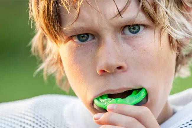Close-up of a young athlete biting a green mouthguard, wearing sports gear outdoors with blurred background