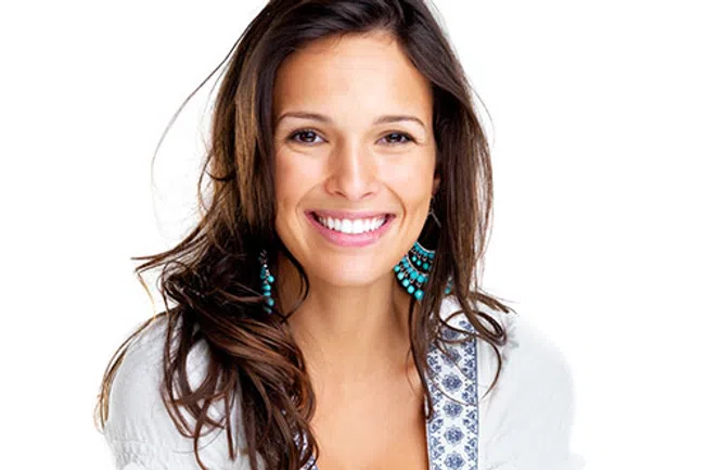 Happy young woman with long brown hair wearing turquoise earrings and a white top smiling at the camera