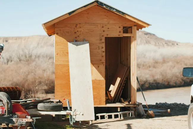 Unfinished wooden shed under construction in a dry, outdoor setting with building materials and tools nearby