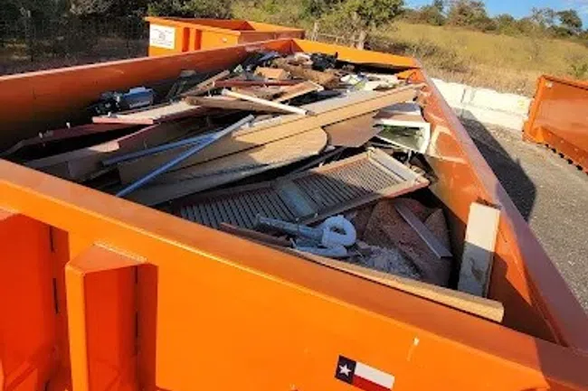 Orange dumpster filled with wood debris and construction waste outdoors on a sunny day.