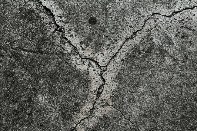 Close-up of cracked, weathered gray concrete surface with rough texture and small debris.