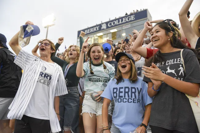 Berry College students cheer loudly at an outdoor event under evening stadium lights.