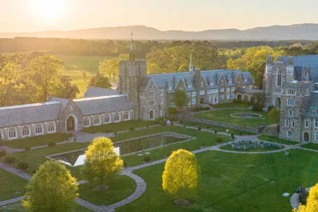 Aerial view of a historic stone campus with green lawns, reflecting pools, and surrounding trees at sunset.