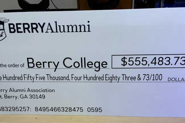 Giant check from Berry Alumni Association to Berry College for $555,483.73 donation displayed on table.
