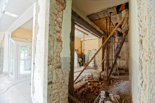 Construction site inside a building with exposed brick walls and worker on scaffolding renovating.