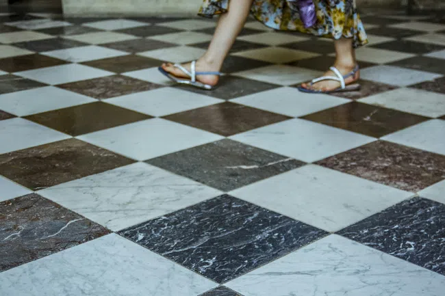 Person wearing sandals walking on a black and white checkered marble floor with a floral dress