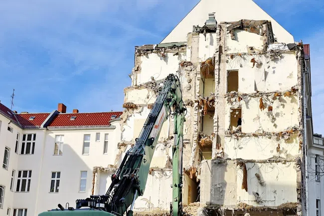 Partially demolished building with construction machinery under blue sky in an urban area.