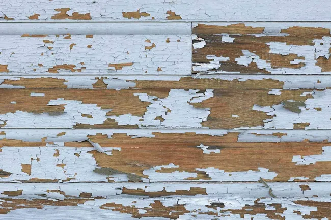 Close-up of wood panels with peeling light blue paint revealing natural brown wood beneath.