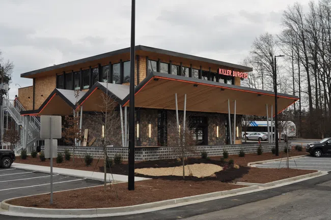 Modern Killer Burger restaurant with sharp angled roof, large windows, and parking lot on a cloudy day