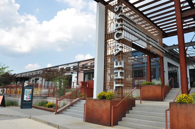 Exterior of a modern building with rust-colored metal structure and stairs under a cloudy sky.