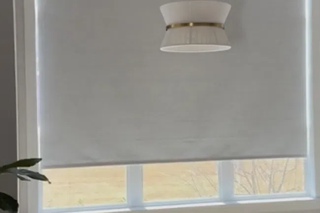 Modern room with a large window covered by a grey roller shade and a white pendant light hanging from the ceiling.