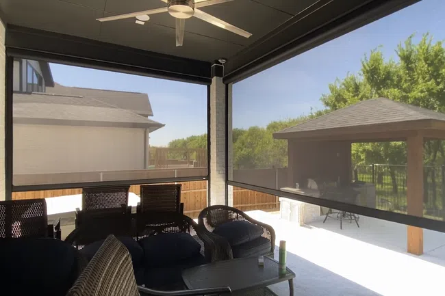 Outdoor patio with wicker furniture, ceiling fan, and retractable mesh screens overlooking backyard and gazebo.