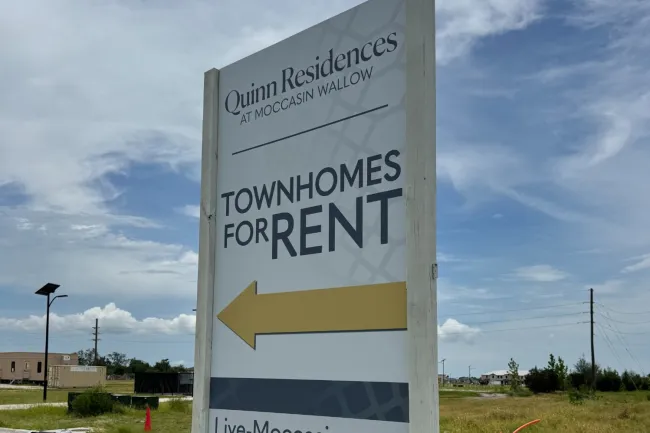 Quinn Residences townhomes for rent sign with arrow and website Live-Moccasin.com on grass roadside.