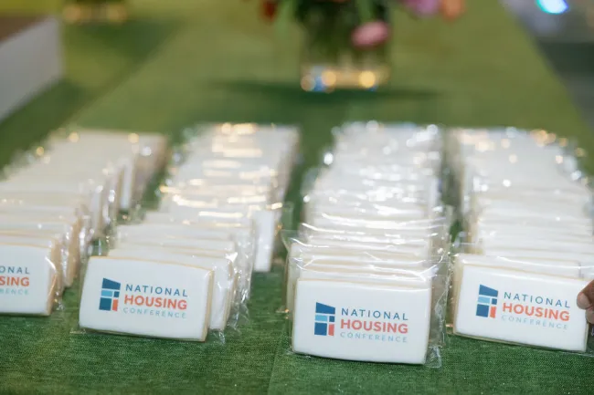 Rows of National Housing Conference branded cookies wrapped in plastic on a green tablecloth.