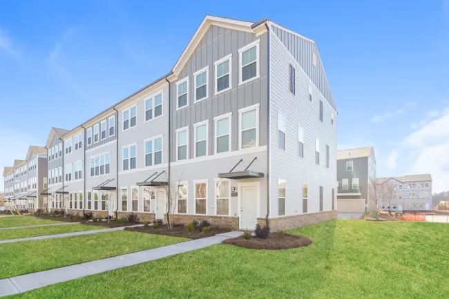 Modern three-story townhouses with gray siding and large windows on a sunny day with green lawns.