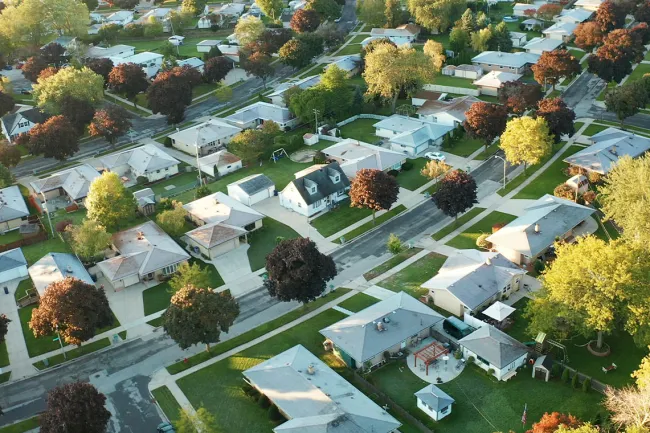 Aerial view of a suburban neighborhood with houses, streets, and trees in early autumn light.