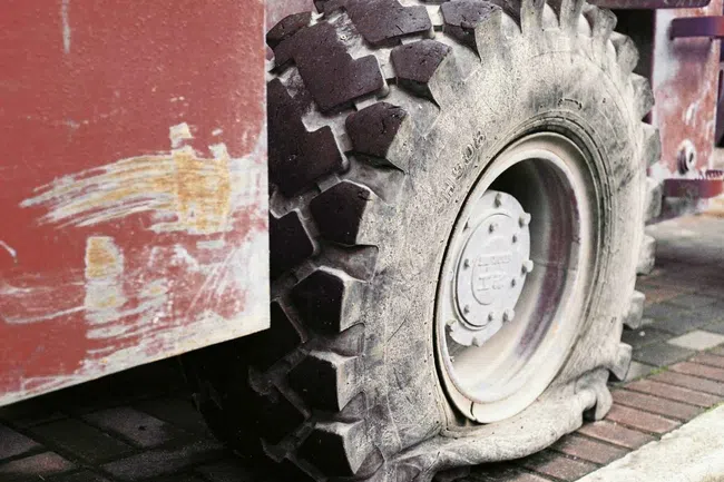 Close-up of a large flat tire on a rugged industrial vehicle with a worn red body and brick pavement.