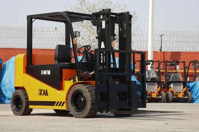 Yellow and black forklift parked outdoors with multiple forklifts visible in the background under clear skies.