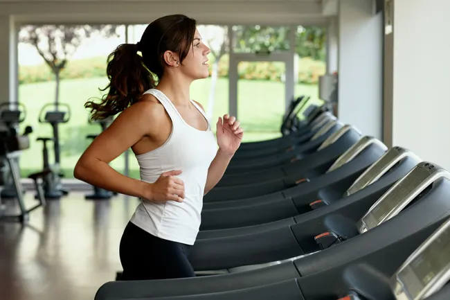 Young woman running on a treadmill in a modern gym with natural light and exercise equipment in the background
