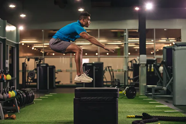 Athlete performing a box jump in a modern gym with fitness equipment and green turf flooring