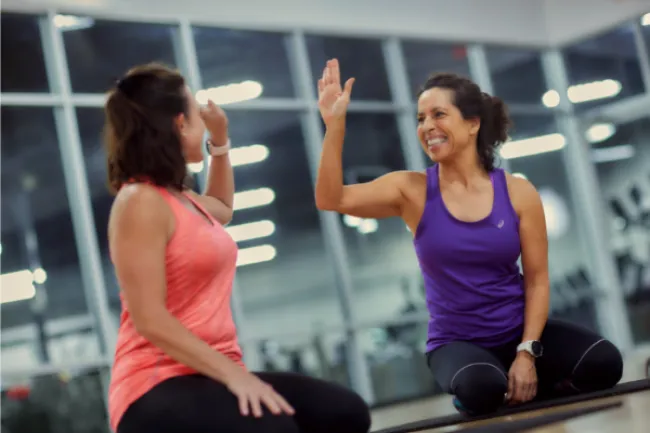 Two women in workout clothes giving a high five during a fitness session at the gym.