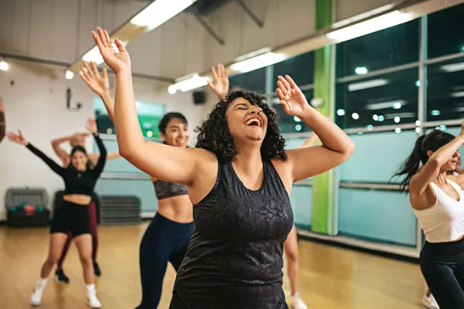 Happy diverse women dancing energetically in a bright fitness studio group exercise class with raised arms.