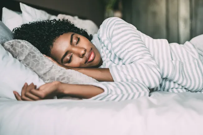 Peaceful young woman sleeping on bed with striped pajamas and soft pillows in cozy bedroom