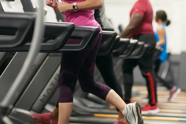 People running on treadmills in a gym wearing athletic clothes and fitness trackers.