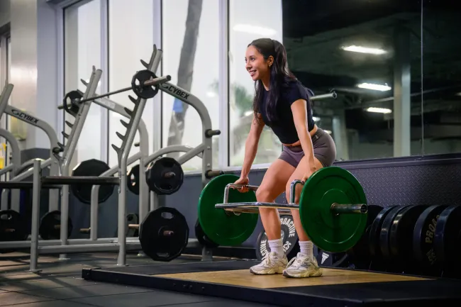 Smiling woman lifting a barbell with green weights in a modern gym setting