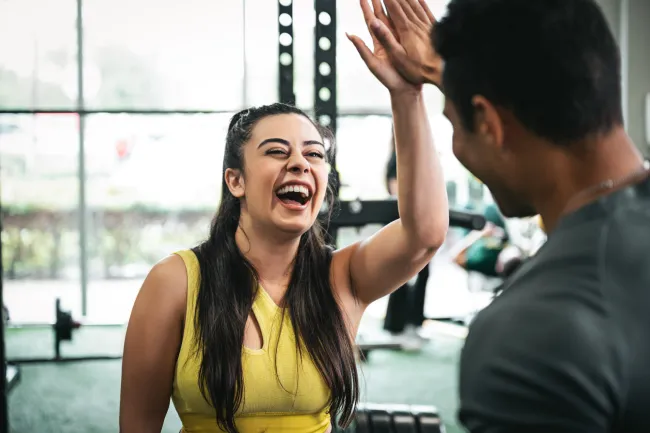 Smiling woman in yellow tank top giving a high five to a man at the gym.